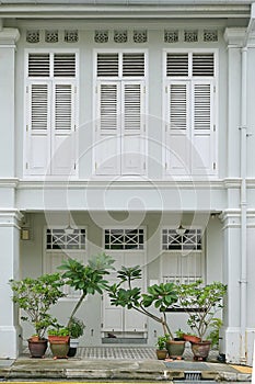 Facade of a conserved Straits Chinese residential terrace house, with white louvered windows and 5-foot passage way