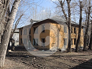 Facade, corner of an old yellow abandoned hut with broken windows among the trees prepared for recycling