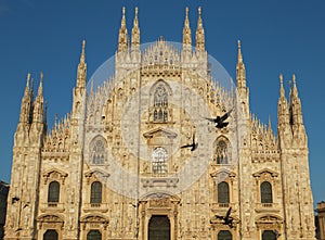 Facade of the Duomo Cathedral in Milan against blue sky, lit by golden setting sun