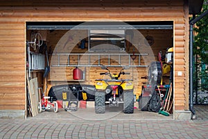 Facade front view open door ATV quad bike motorcycle parking messy garage building with wooden siding at home driveway backyard