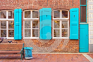 Facade of German house. Windows with blue shutters. Blue door. Blue trash can. Wooden bench.