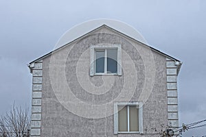 Facade of a gray house with two windows against the sky