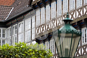 Facade of a half-timbered house in an old town, with a deliberately blurred lantern and a blurred crown of trees in the foreground