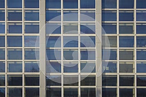 Facade of high glass modern building with square windows and a reflection of blue sky