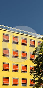 Facade of a hotel or office building from the 60s, plaster with yellow paint and sunblinds extended in bright red with an