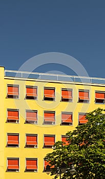 Facade of a hotel or office building from the 60s, plaster with yellow paint and sunblinds extended in bright red with an