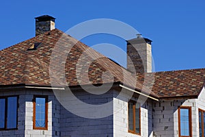 Part of the house of gray brick with windows under a brown tiled roof against the blue sky