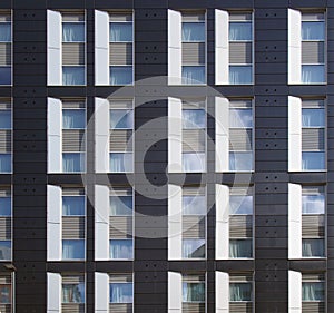 Facade of a large black and white modern commercial building with repeating windows and geometric panels