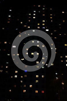 Facade of a large multi-storey block of flats with many lighting windows in apartments night view