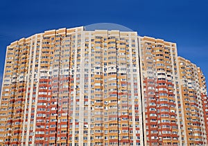 Facade of a large multi-storey block of flats with many windows over cloudless blue sky front view