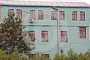 Facade of a large old green house with a row of brown windows