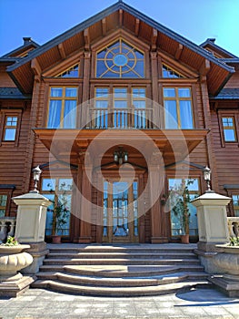 Facade of a large wooden two-story luxury cottage with marble stairs and street lamps