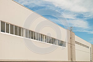 Facade of a long multi-span industrial building under a blue cloudy sky