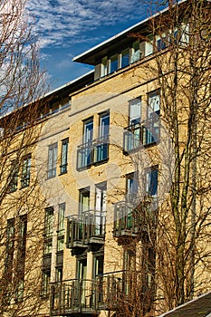 Facade of a modern apartment building with balconies, framed by leafless trees against a clear blue sky in Harrogate, England