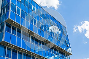 Facade of a modern building. Glass Windows reflected the sky and clouds. Blue gamma