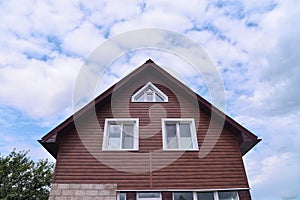 Facade of modern house covered with Siding on blue cloudy sky background. House repairing and construction.