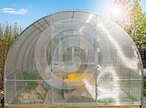Facade of a modern polycarbonate greenhouse on a private plot against a blue sky, spring, outdoors