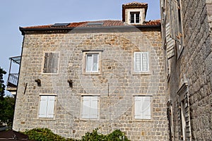 Facade of a multi-storey old stone house. The windows are covered with wooden shutters. Old Town of Budva. Montenegro