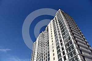 Facade of a new modern high-rise residential building. Skyscraper on blue sky background.  Tall house renovation project,