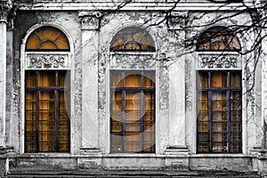 Facade of old abandoned building with three large arched windows of orange glass. Monochrome background