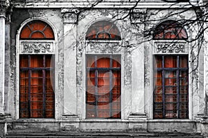 Facade of old abandoned building with three large arched windows of the red glass. Monochrome background