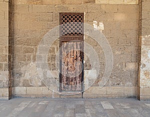 Old abandoned stone bricks wall with one weathered wooden door and wooden grid window, Old Cairo, Egypt