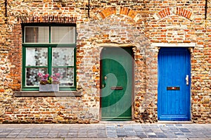 The facade of an old brick house with a window and two wooden doors