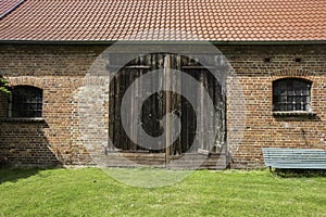 A Facade of an old brick walls barn with tiled roof, and wooden door