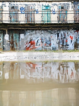 Facade of old building full of paintings reflected in puddle