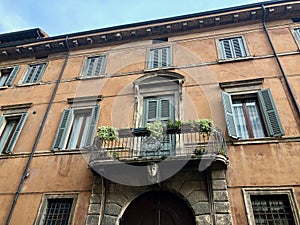 Facade of old european house, windows with shutters and balcony decorated green plants and flowers in pots in Verona, Italy