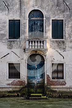 Facade of old house with vintage blue door and windows, on a canal in Venice, Italy