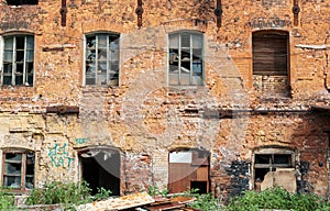 Facade of the old red brick building with broken windows and traces of vandalism