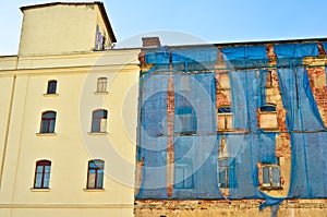 The facade of an old ruinous building is mantled with some blue curtains to protect the pedestrians