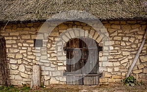 Facade of an old stone brick wall with wooden doors, a small window and thatched roof