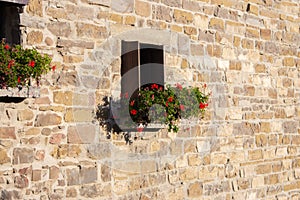 Facade of old stone house with flowers. Traditional exterior of ancient building in sunlight. Windows with flower in village.