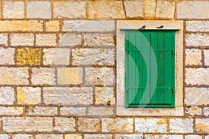The facade of an old stone house with a window with green shutters.