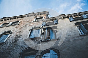 Facade of an old Venetian brick building with an open window and a clear blue sky, Venice, Italy