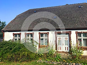 Facade of an old village house in Poland with overgrown front yard garden.