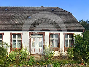 Facade of an old village house in Poland with overgrown front yard garden.