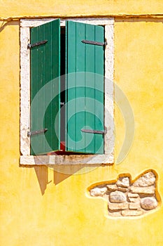 Facade of an old yellow house with windows with green shutters.