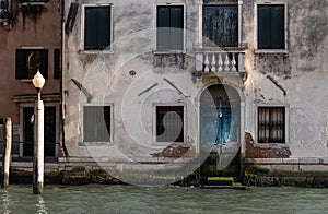 Facade of partially mossy old house with wooden blue vintage door on a canal in Venice, Italy