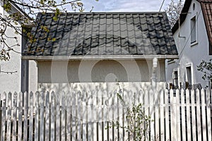 The facade of a private house with a gray wall under a green tiled roof behind a white fence