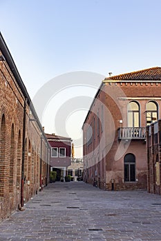 the facade of a red building with arched windows in Murano in Venice against a blue sky