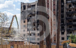 Facade of a residential abandoned multi-storey building after a strong fire. A construction excavator with a hydraulic crusher