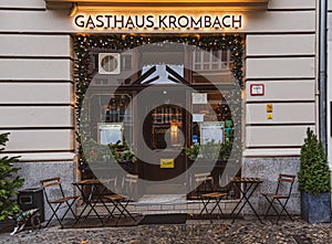 Facade of retro restaurant with Christmas decorations in front of entrance and empty tables and wooden chairs.