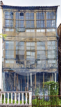 Facade in ruins and about to collapse from a very old wooden house with large galleries and a net protecting from falls in a town