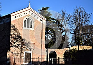 Facade of the Scrovegni Chapel and many trees, illuminated by the sun, the left side in the shade in Padua.