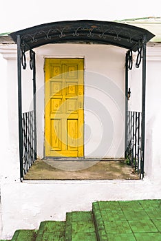 The facade of a small house with white walls, a yellow door and a green staircase. City space, architecture