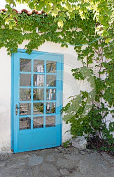 Facade of traditional white greek house with blue door and window and reflected on glass