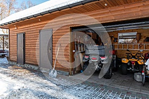 Facade view open door ATV home garage with quad bikes offroad vehicle parked sunny snowy cold winter day. ATV adventure